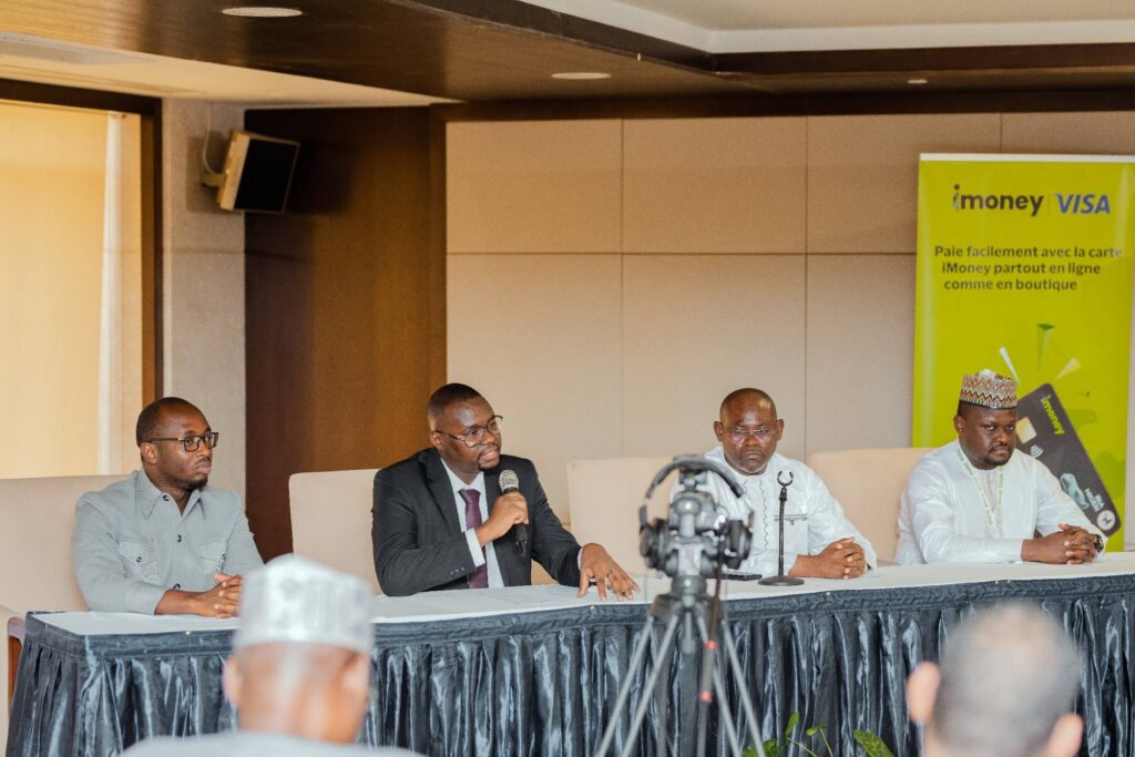 Conférence de presse à Niamey pour le lancement de la carte Visa iMoney. Quatre intervenants, dont Sidikou Boubacar d'iFutur au micro, sont assis à une table face aux journalistes, à côté d'un kakemono publicitaire vert.