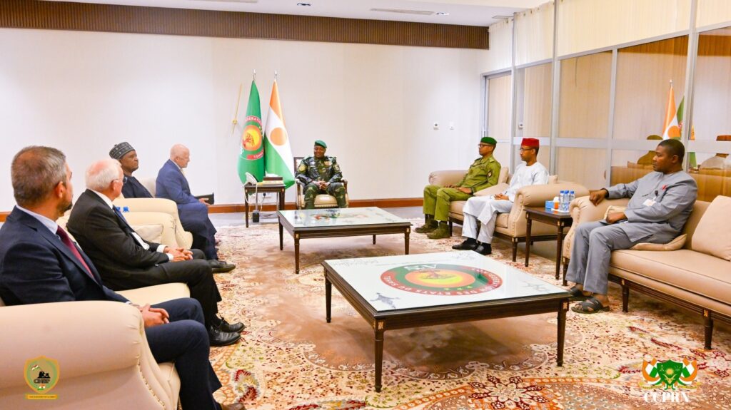 Le Président du Niger, le Général d’Armée Abdourahamane Tiani, et le PDG de Global Atomic, Stephen G. Roman, discutent autour d'une table de réunion à la Présidence. Ils sont entourés de collaborateurs civils et militaires lors d'une séance de travail officielle portant sur le projet minier de Dasa.