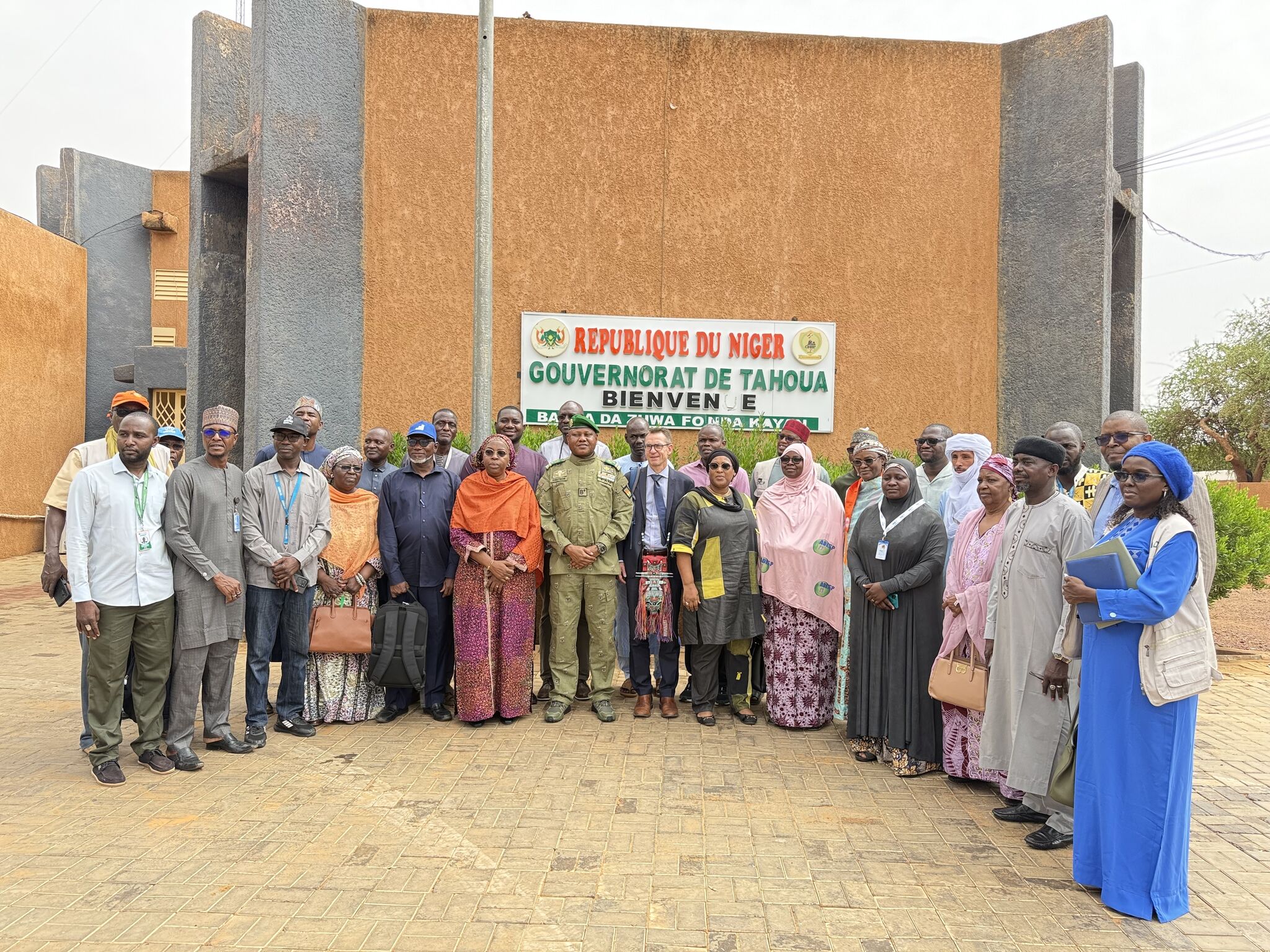 Photo de groupe officielle devant le bâtiment du Gouvernorat de Tahoua au Niger, réunissant Brian J. Williams (PBSO/PBF), le Gouverneur en tenue militaire, et la délégation de la HACP, des Nations Unies et des ONG partenaires pour la consolidation de la paix.