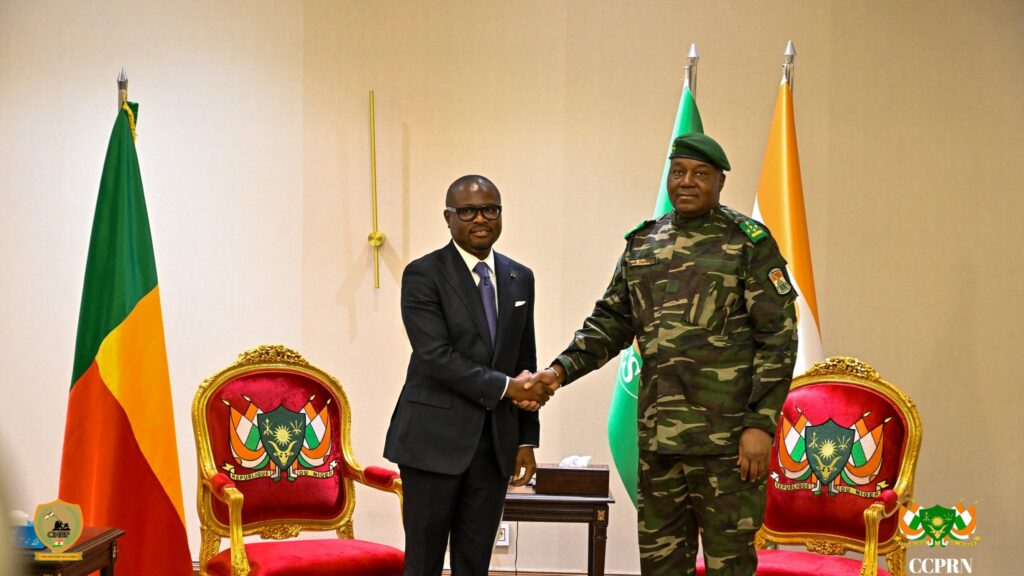 Poignée de main officielle entre le président du Bénin Romuald Wadagni en costume sombre et le président de la transition du Niger le général Abdourahamane Tiani en tenue militaire, devant les drapeaux de leurs pays respectifs à Niamey.