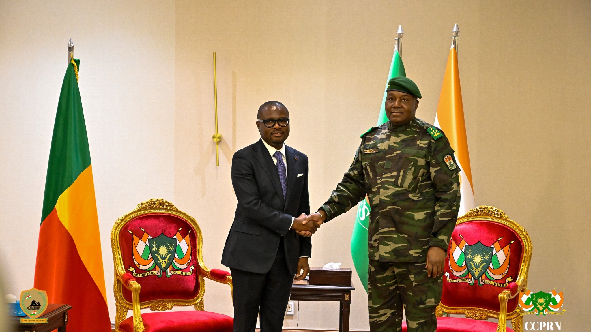 Poignée de main officielle entre le président du Bénin Romuald Wadagni en costume sombre et le président de la transition du Niger le général Abdourahamane Tiani en tenue militaire, devant les drapeaux de leurs pays respectifs à Niamey.