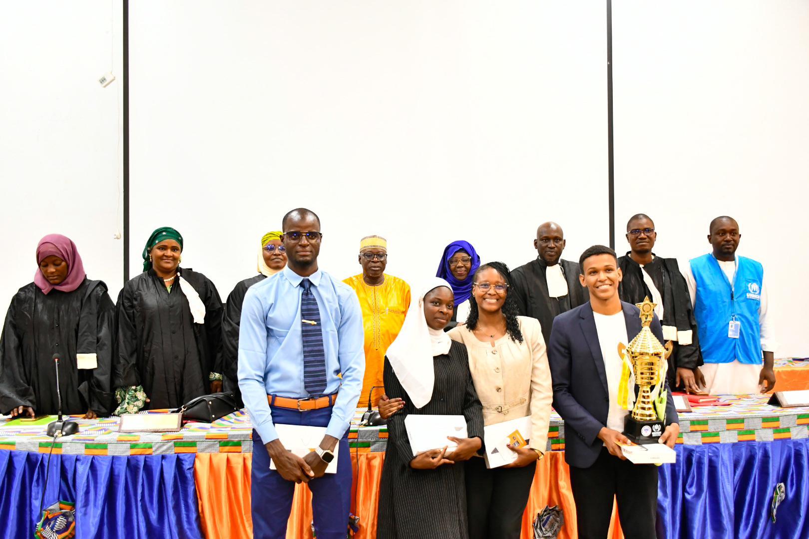 Photo de groupe officielle de l'équipe gagnante de l'Université Abdou Moumouni de Niamey (UAM) posant fièrement avec leur trophée, entourée des membres du jury en robe d'avocat et des partenaires humanitaires lors de la finale du Concours National de Plaidoirie 2026.